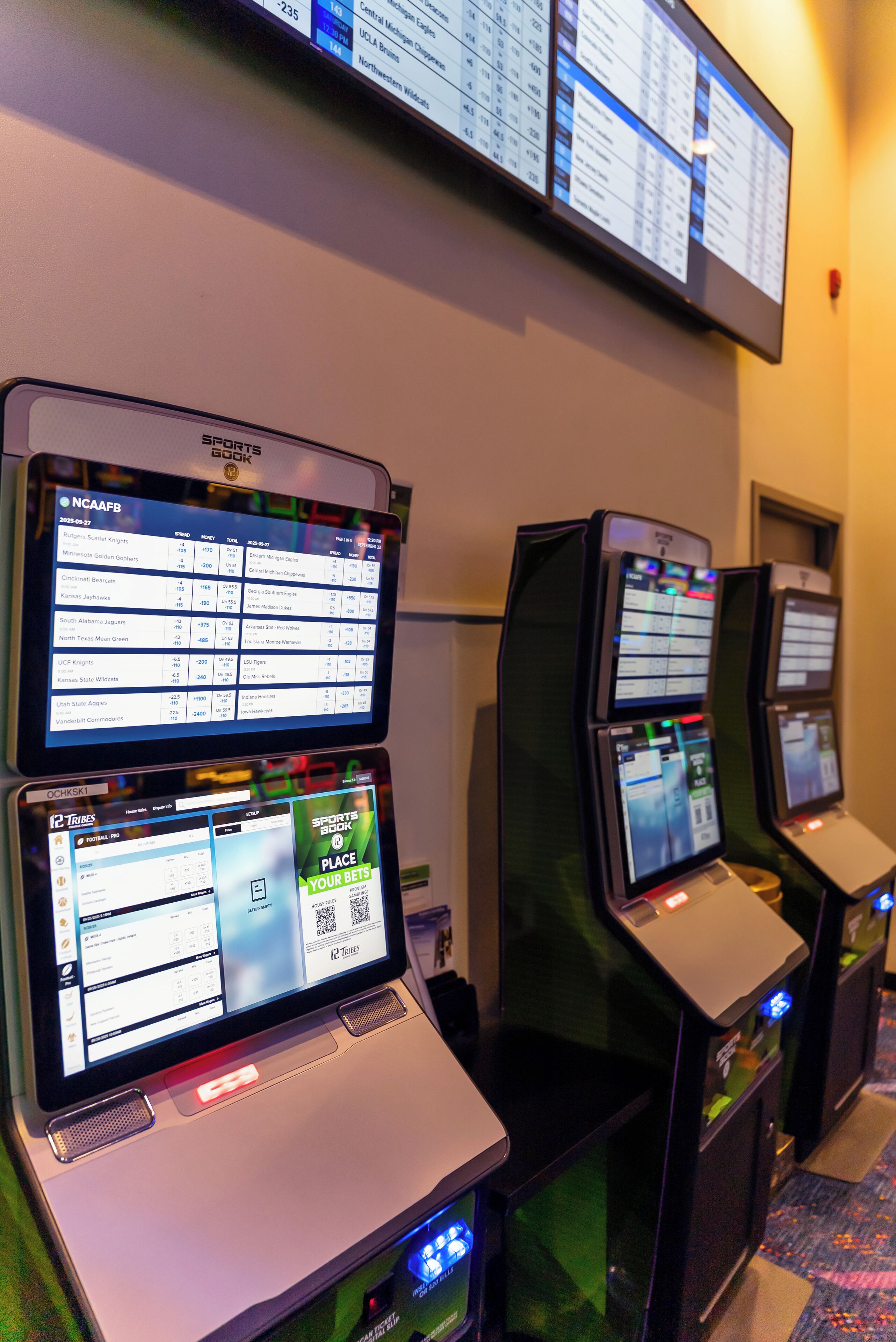A row of gaming machines with screens displaying sports betting information.