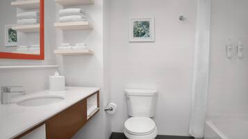 A modern bathroom with a white sink, mirror, and toilet. There are shelves with folded towels and a framed picture on the wall.