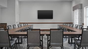 Une salle de conférence avec une longue table, de nombreuses chaises, un téléviseur à écran plat et une moquette à motifs.