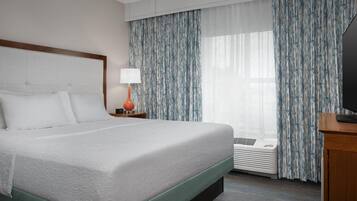 Quarto de hotel com uma cama grande, mesa de cabeceira com abajur, televisão e janela com cortinas.