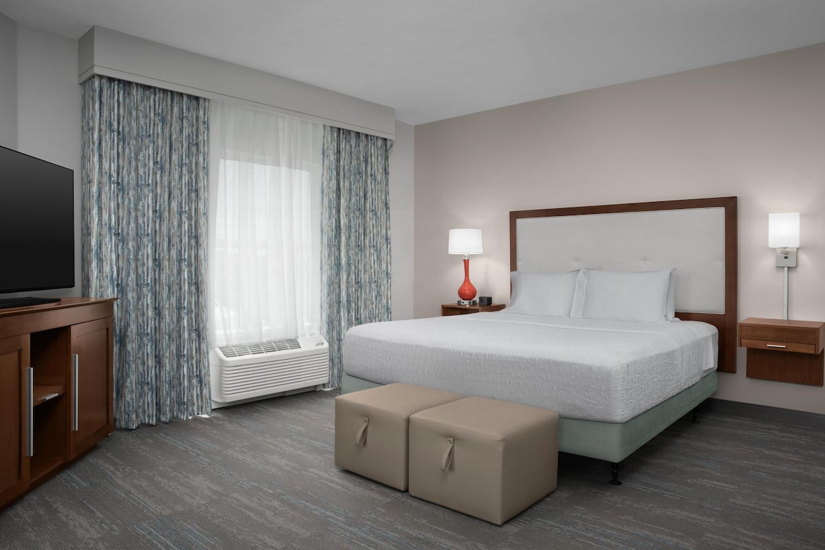 Ein Hotelzimmer mit Bett, Nachttischen, Fernseher, Heizung und einem mit Vorhängen versehenen Fenster.