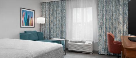A hotel room with a bed, a desk, a chair, a lamp, and a large window with curtains.