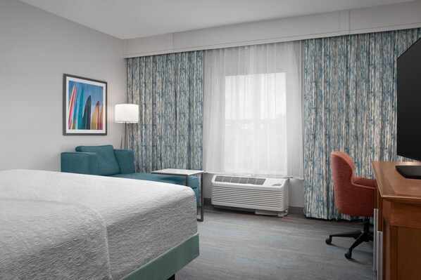 A hotel room with a bed, a desk, a chair, a lamp, and a large window with curtains. - Hampton Inn & Suites Vero Beach Downtown (Vero Beach)
