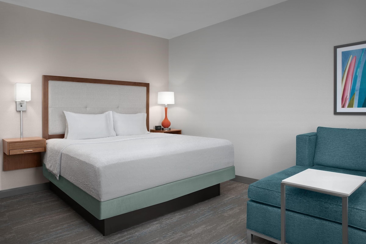 Ein Hotelzimmer mit Bett, Nachttischen, einem Sessel und einem kleinen Tisch.