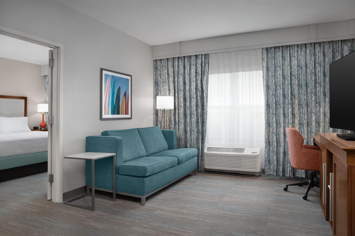 Ein Hotelzimmer mit Bett, einer Couch, einem Fernseher, einem Schreibtisch und einem Fenster mit Vorhängen.