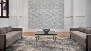 Una sala de estar moderna con un sofá, una mesa de centro de vidrio con un cuenco y una pared con textura.