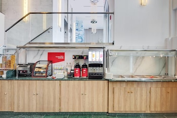 A modern office space with a flat-screen TV mounted on a wall with a winter forest mural, a laptop on a desk, a white chair, and a coffee machine. at Wyndham Garden Brooklyn Sunset Park