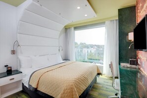 A modern hotel room with a large bed, a desk with a lamp, a TV, and a view of the city. - Wyndham Garden Brooklyn Sunset Park (Brooklyn)