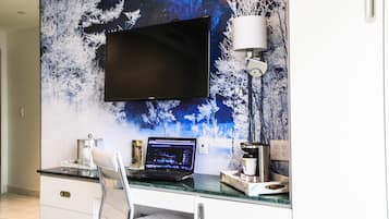 A modern office space with a flat-screen TV mounted on a wall with a winter forest mural, a laptop on a desk, a white chair, and a coffee machine.