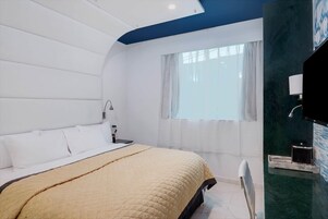 Egy modern hálószoba, amelyben található egy ágy, egy éjjeliszemélyzet, ablakfüggönnyel ellátott ablak, valamint egy fürdőszoba tükörrel és mosdókagylóval, és egy kék színű, a térbe beillesztett díszítőfal.