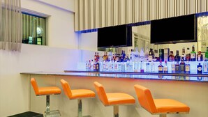 Zona de bar con una barra larga, varias botellas de licor y tres taburetes naranjas.