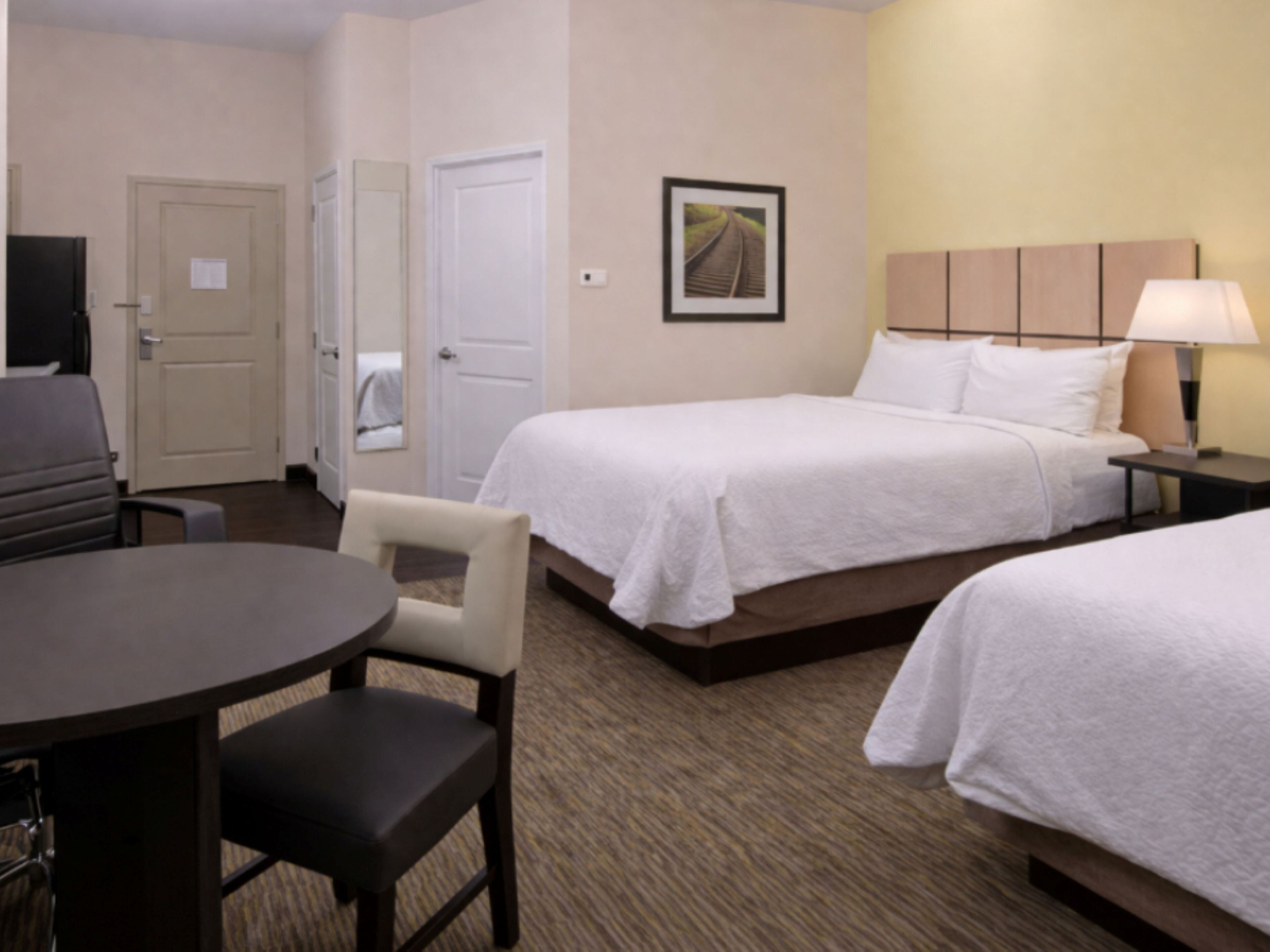 A hotel room with two beds, a desk, a chair, a television, and a lamp.