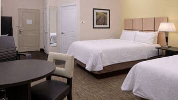 A hotel room with two beds, a desk, a chair, a television, and a lamp.