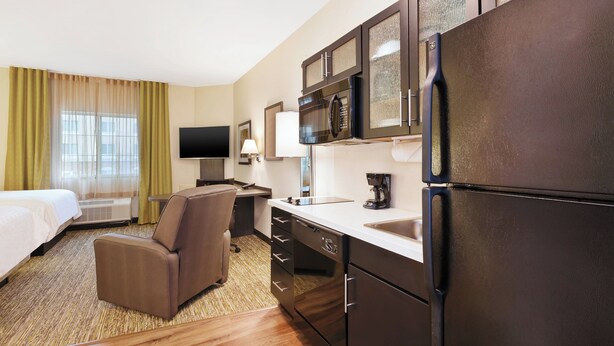 A hotel room with a bed, a sofa, a desk, a refrigerator, a microwave, a sink, and a television. - Candlewood Suites MORGANTOWN-UNIV WEST VIRGINIA by IHG (Morgantown)