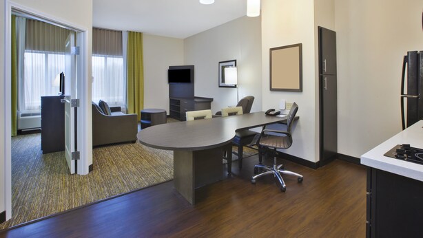 A hotel room with a conference table, chairs, a TV, a refrigerator, and a kitchenette. - Candlewood Suites MORGANTOWN-UNIV WEST VIRGINIA by IHG (Morgantown)