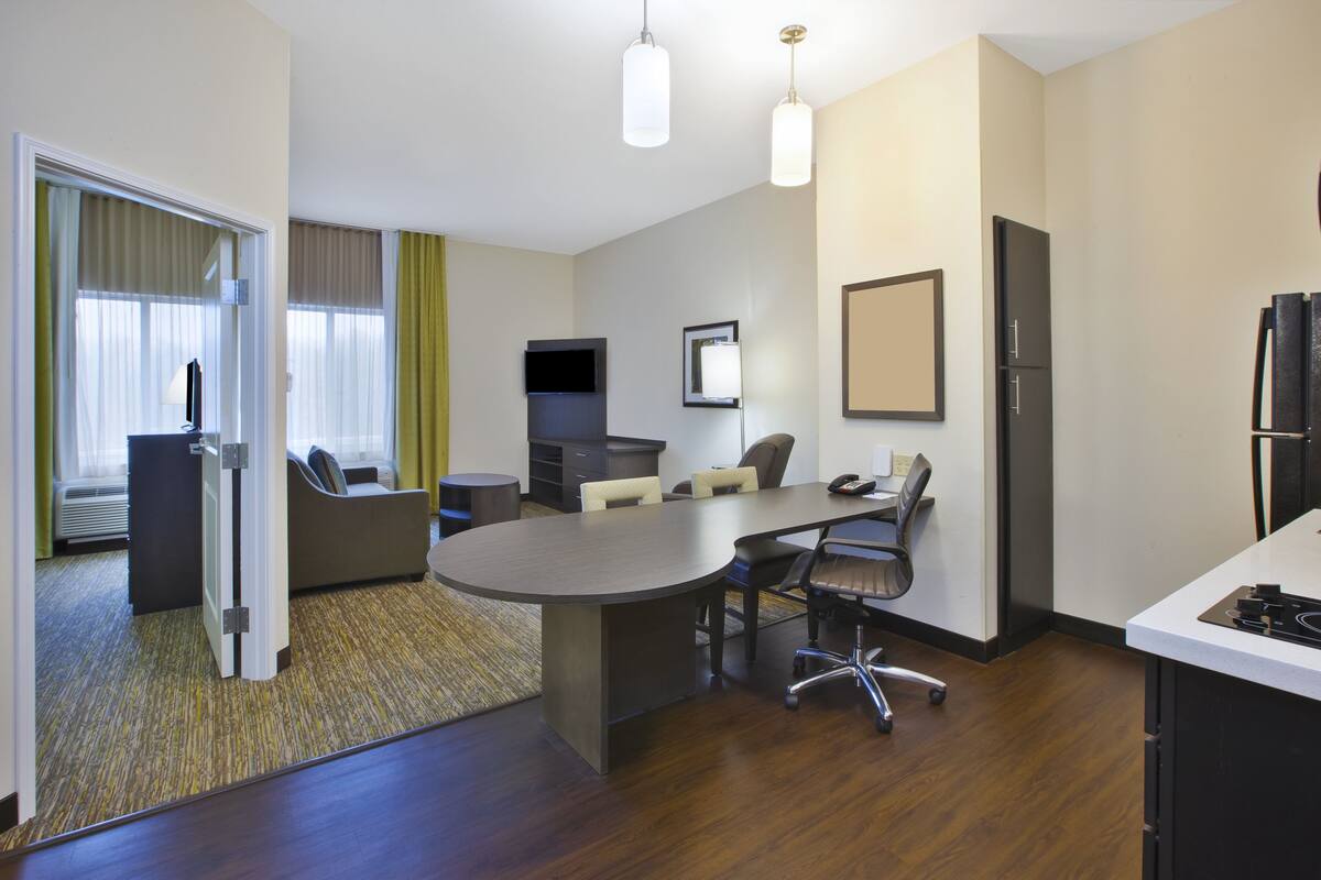 Ein Hotelzimmer mit Konferenztisch, Stühlen, Fernseher, Kühlschrank und einer Küchenzeile.
