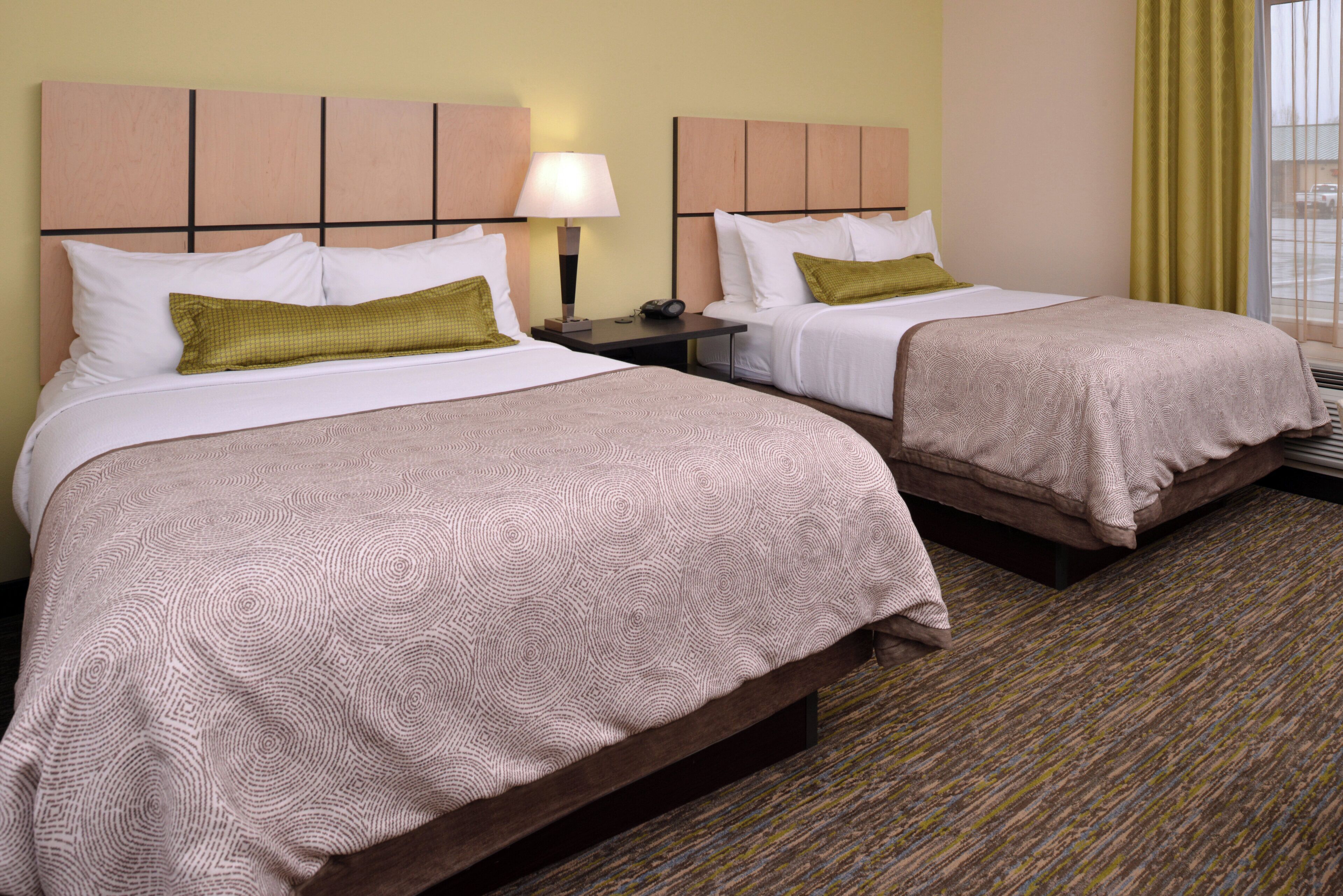 A hotel room with two beds, a nightstand with a lamp, and a window with curtains.