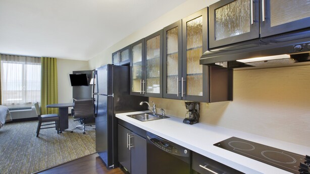 A compact hotel kitchen with a refrigerator, stove, and dishwasher. - Candlewood Suites MORGANTOWN-UNIV WEST VIRGINIA by IHG (Morgantown)