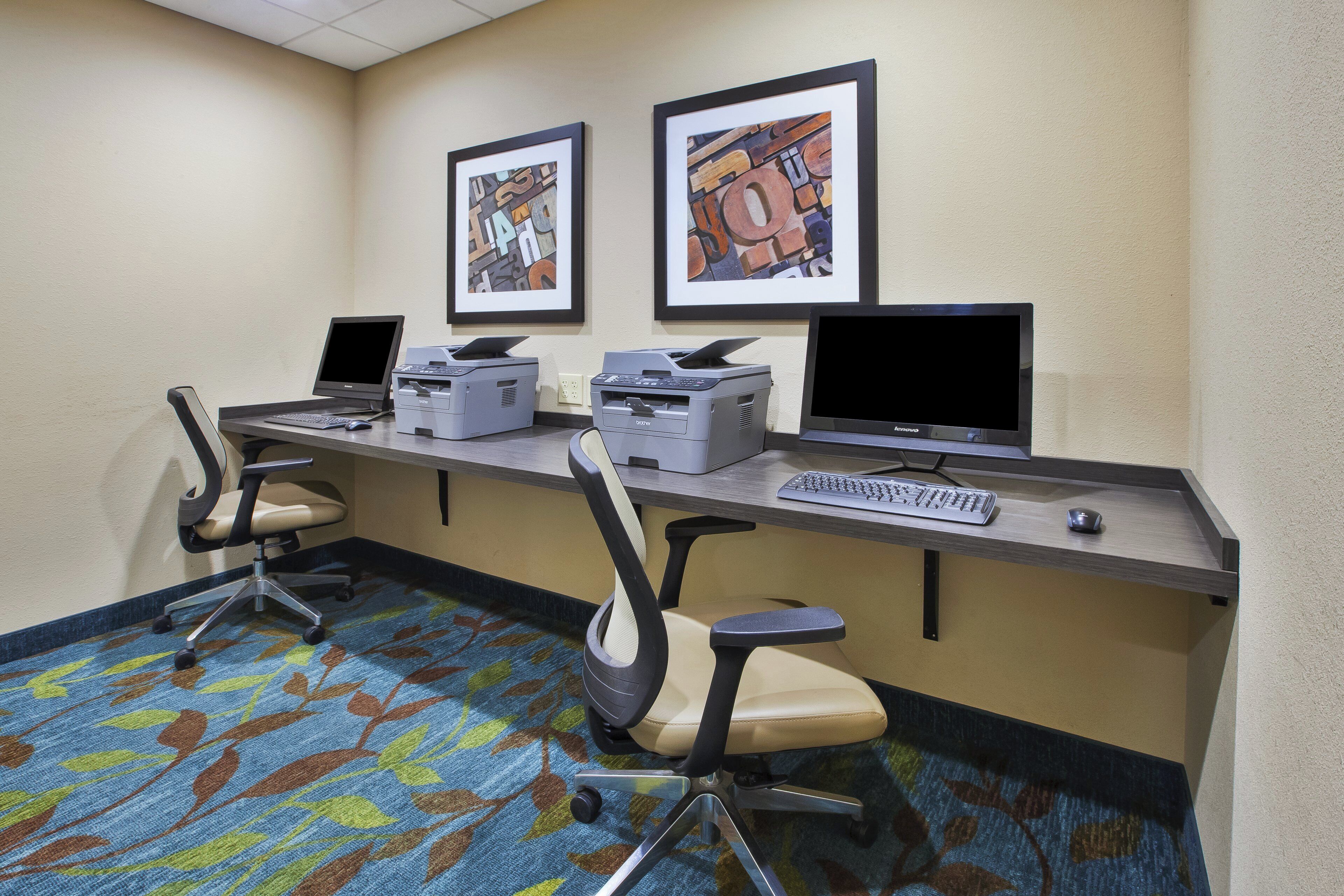A hotel workspace with two desks, computers, printers, and office chairs.
