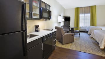 A compact hotel room with a kitchenette, a single bed, a small desk, and a chair.