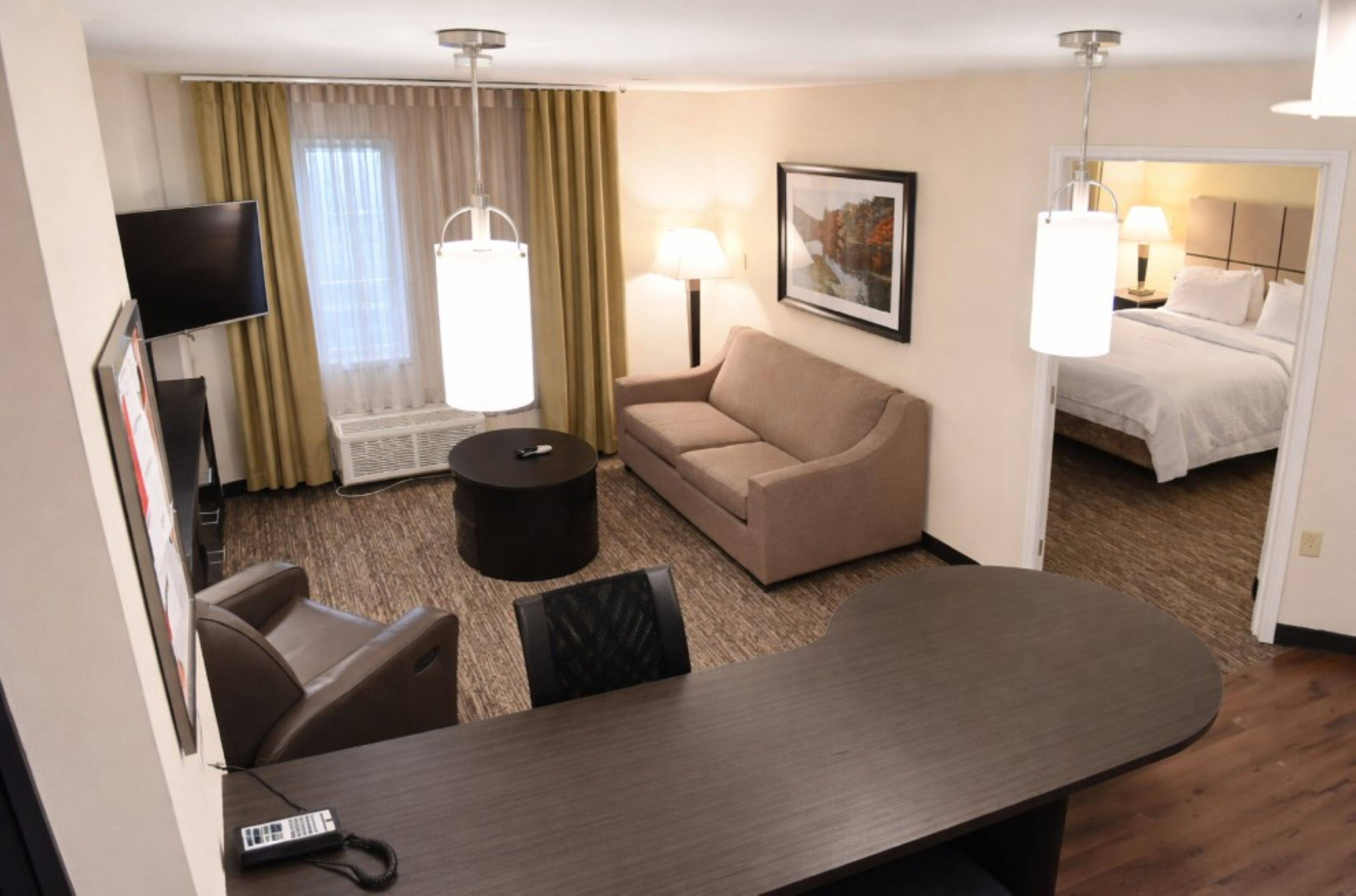 A hotel room with a sofa, a small round table, a TV, a lamp, and a bed.