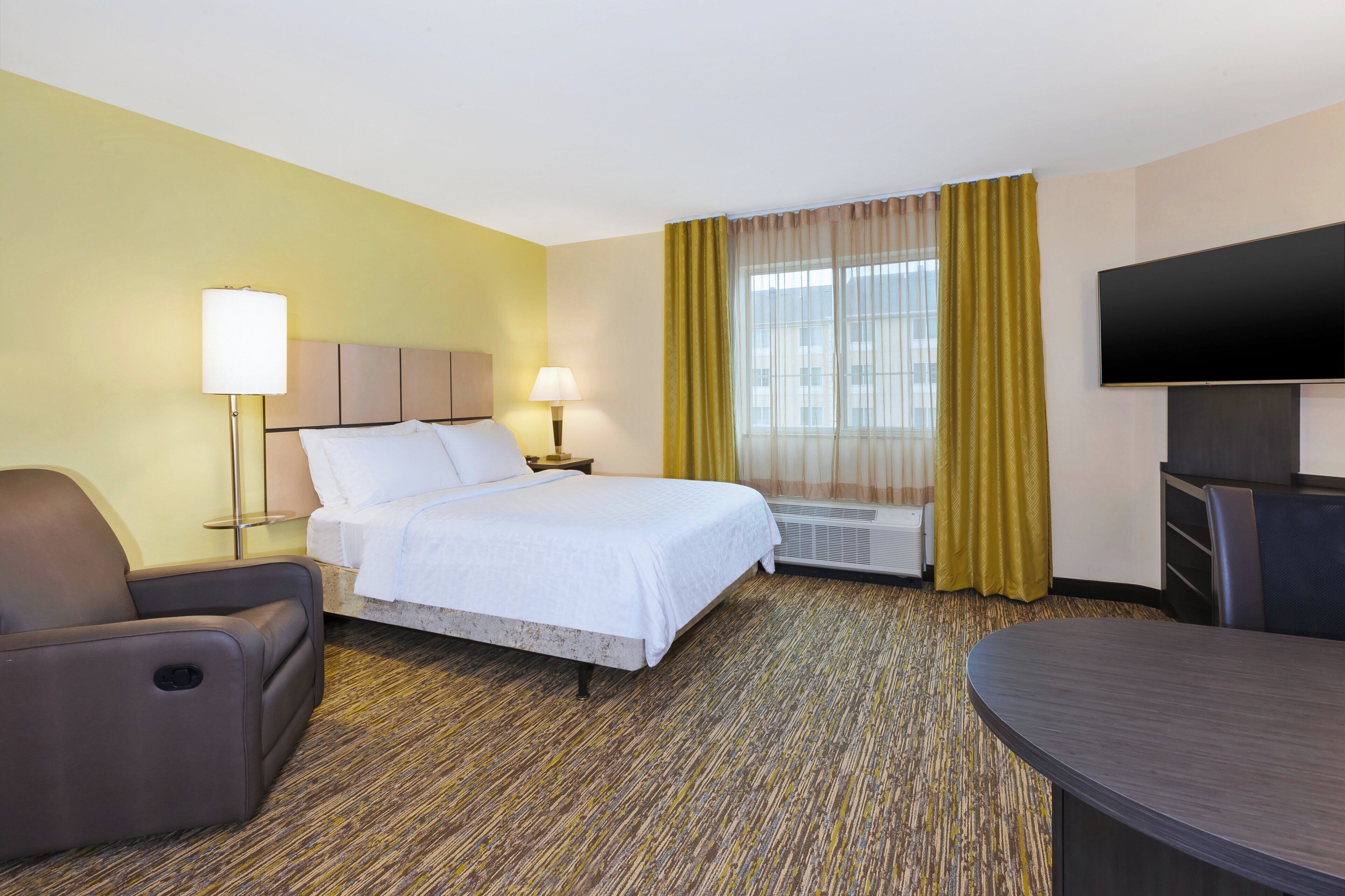 Hotelkamer met een bed, een bureau, een stoel, een flatscreen-tv en een raam met gordijnen.