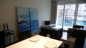 A modern living room with a dining area, a television, and artwork on the walls. - White Princess (Koksijde)