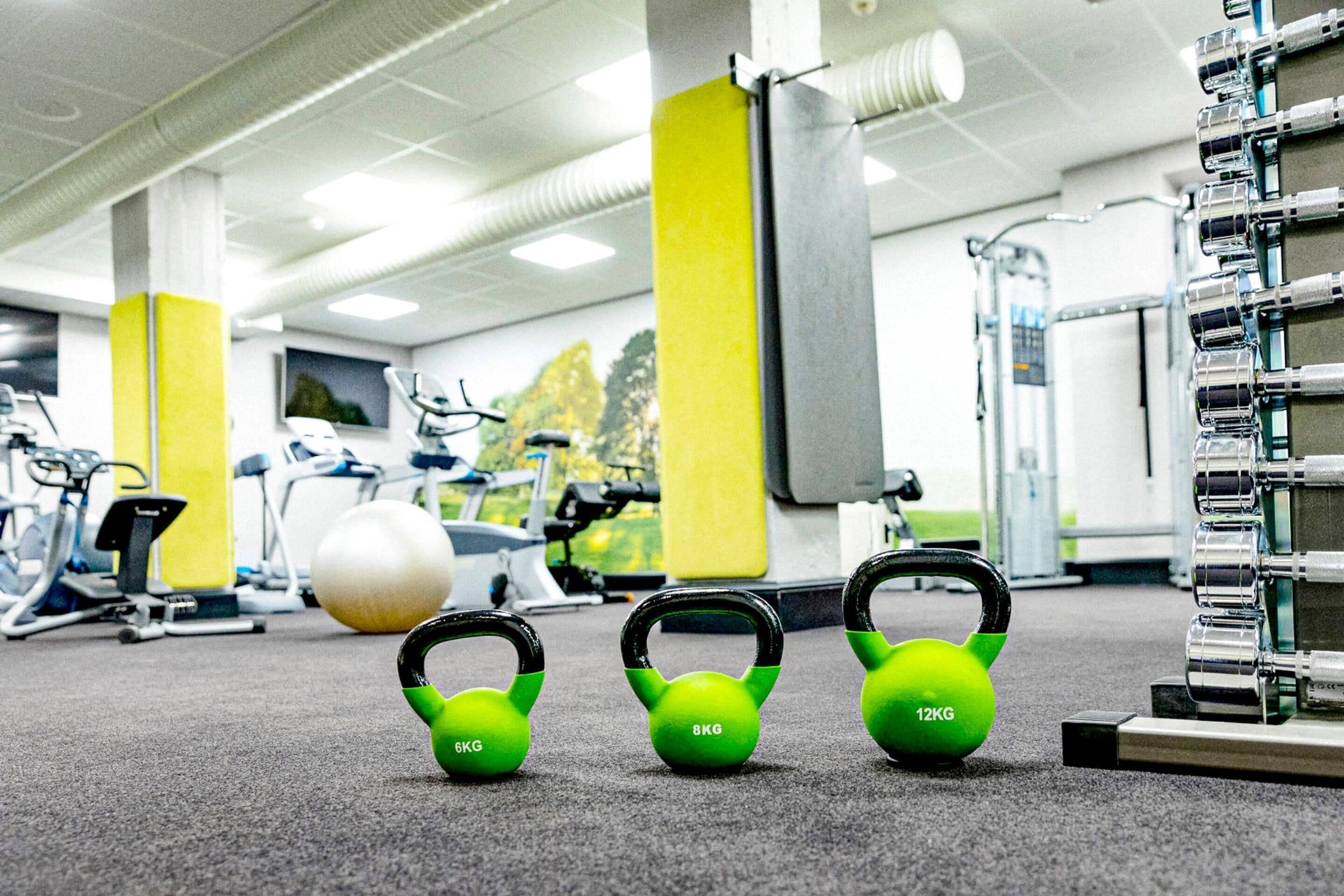 A gym with exercise equipment including kettlebells, a ball, and a treadmill.