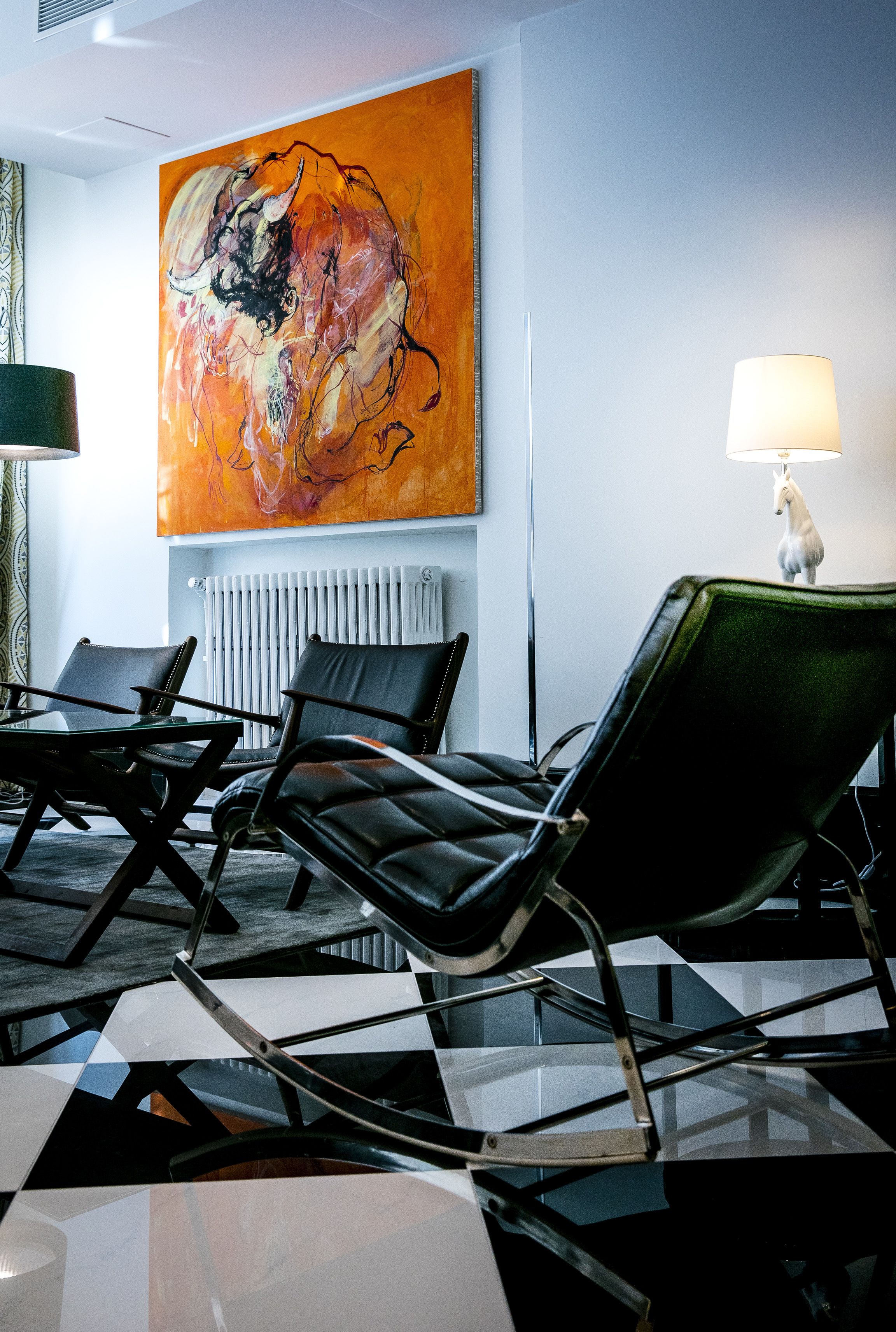 A modern hotel room with a large abstract painting, a radiator, and a lamp with a white horse design.