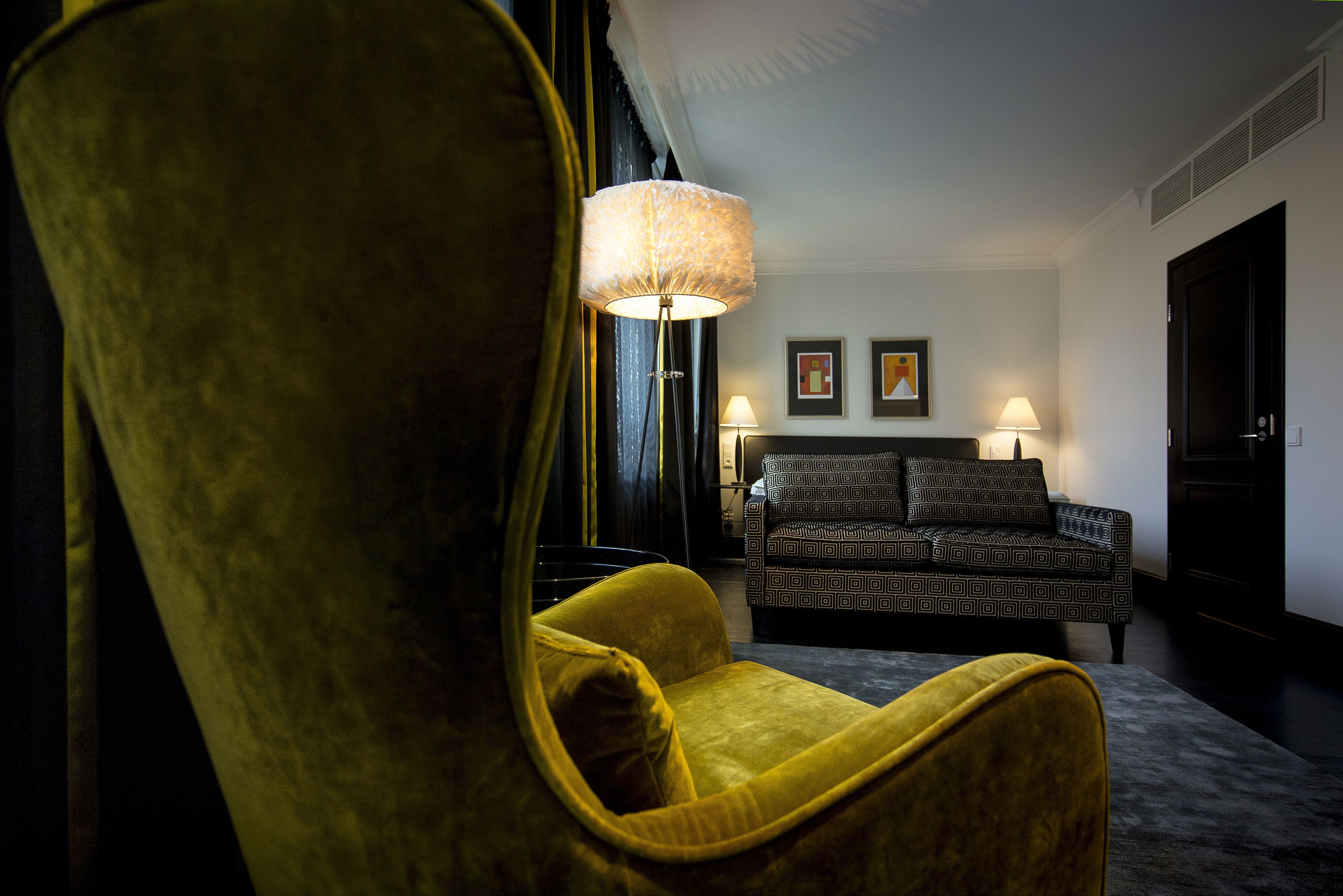 Une pièce avec un fauteuil jaune, un canapé à motifs et un lampadaire.