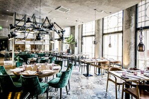 A spacious dining area with multiple tables and chairs, large windows, and hanging pendant lights. - Hotel Lilla Roberts (Helsinki)