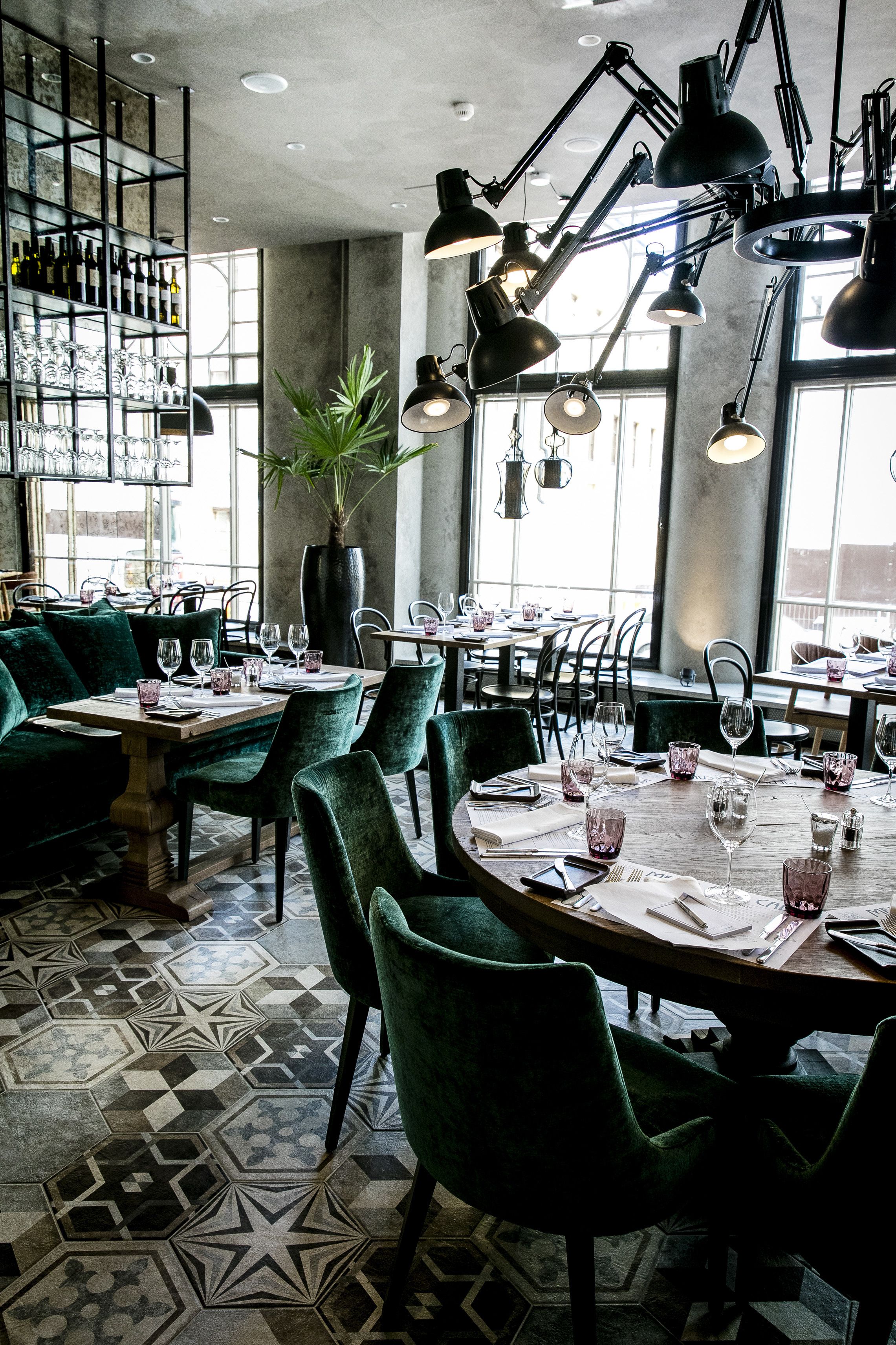 Un restaurante con sillas tapizadas de verde, piso estampado e iluminación colgante.