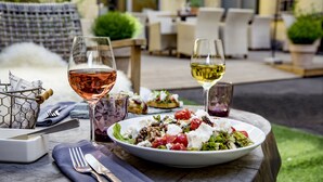 Un área de comedor al aire libre con una mesa dispuesta para dos personas, con una ensalada y copas de vino.