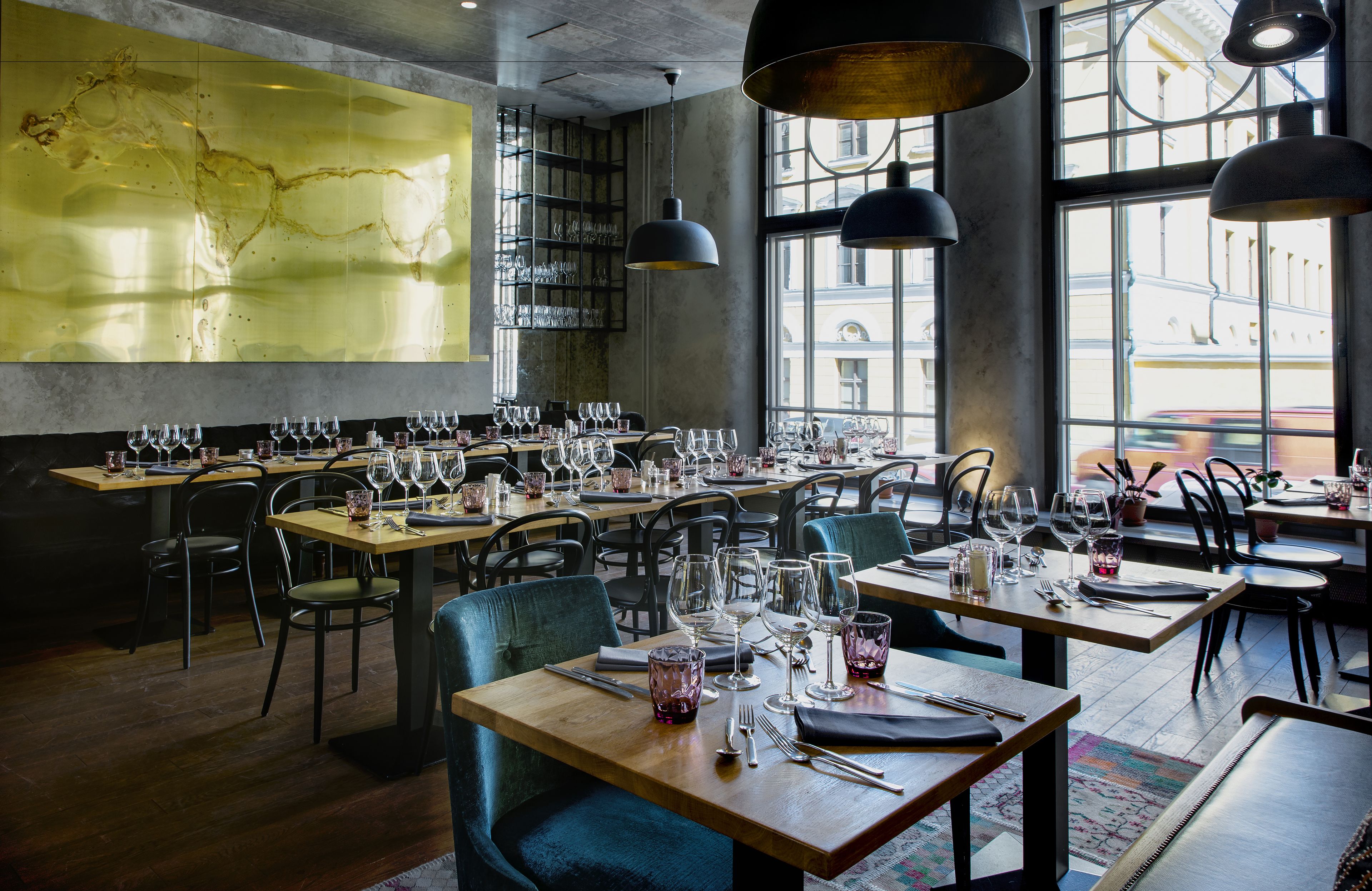 Un restaurante con varias mesas preparadas para comer, ventanas amplias y lámparas colgantes.