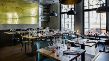 Un restaurante con varias mesas preparadas para comer, ventanas amplias y lámparas colgantes.