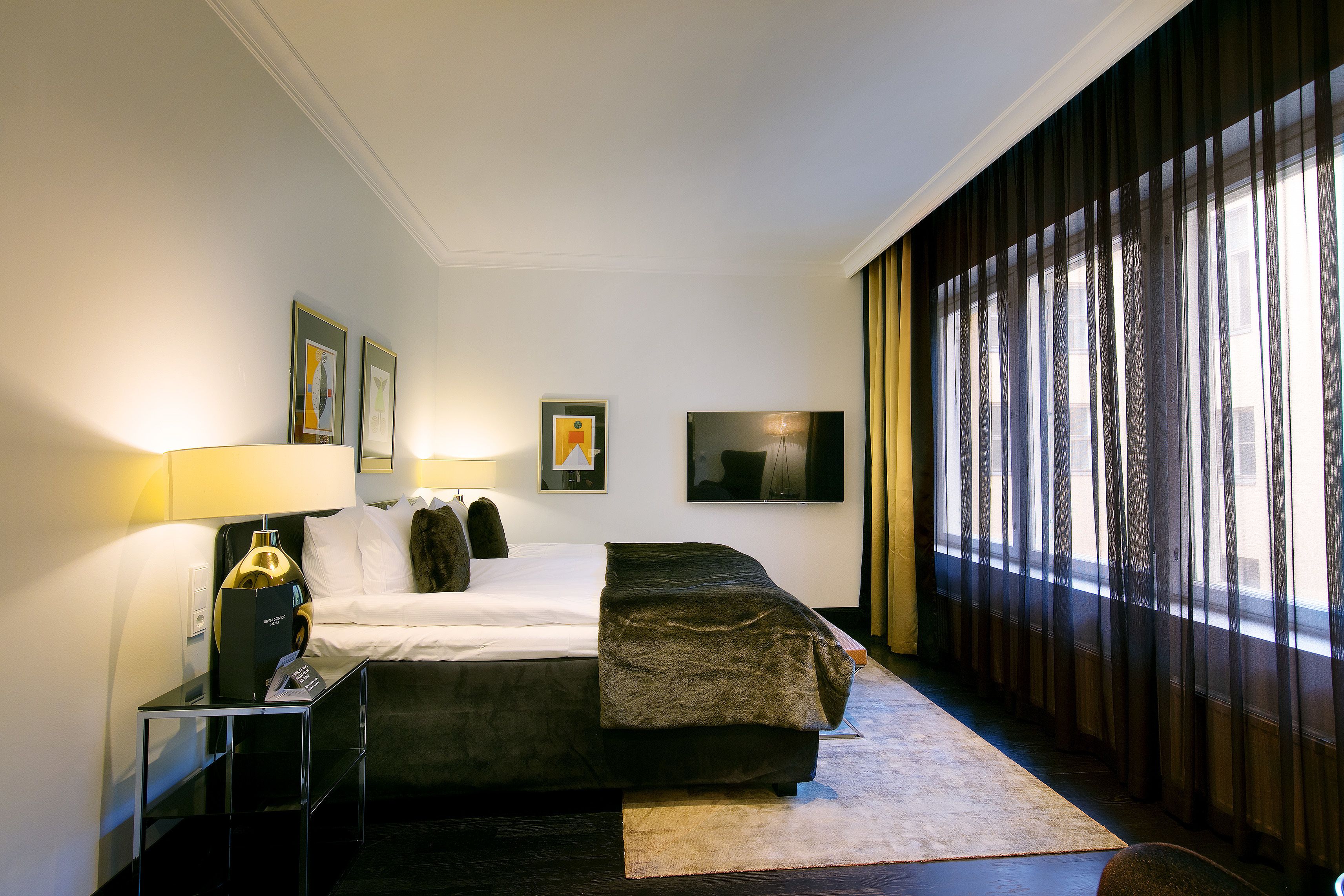 Una habitación de hotel con cama, mesita de noche, lámpara y obras de arte en las paredes.