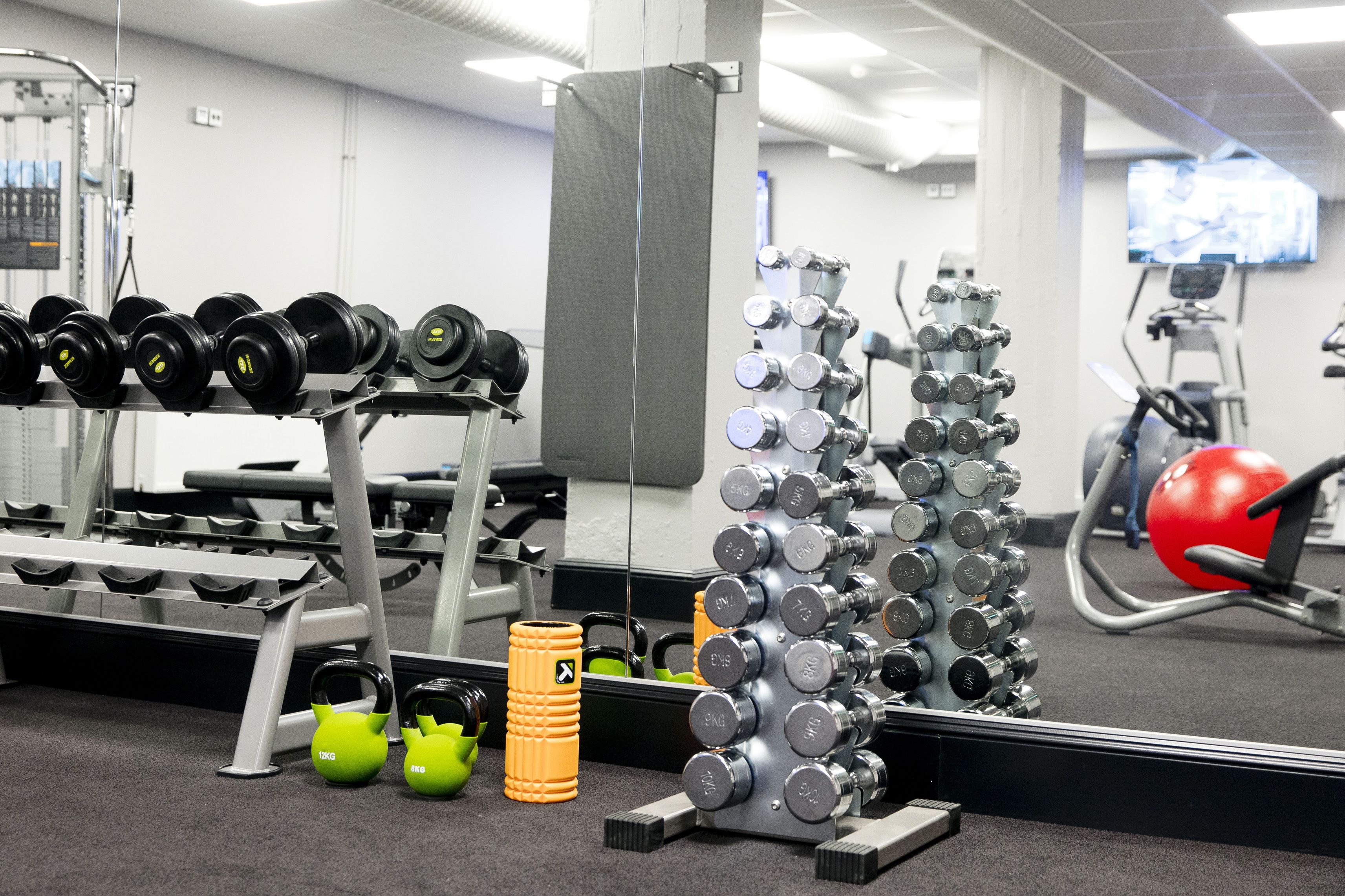 A gym with various exercise equipment, including dumbbells, kettlebells, and a red exercise ball.