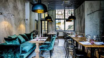 A modern dining area with a long wooden table, blue velvet chairs, and pendant lighting.