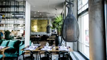 Un restaurante con mesas y sillas, una zona de bar con estantes llenos de botellas y lámparas colgantes.