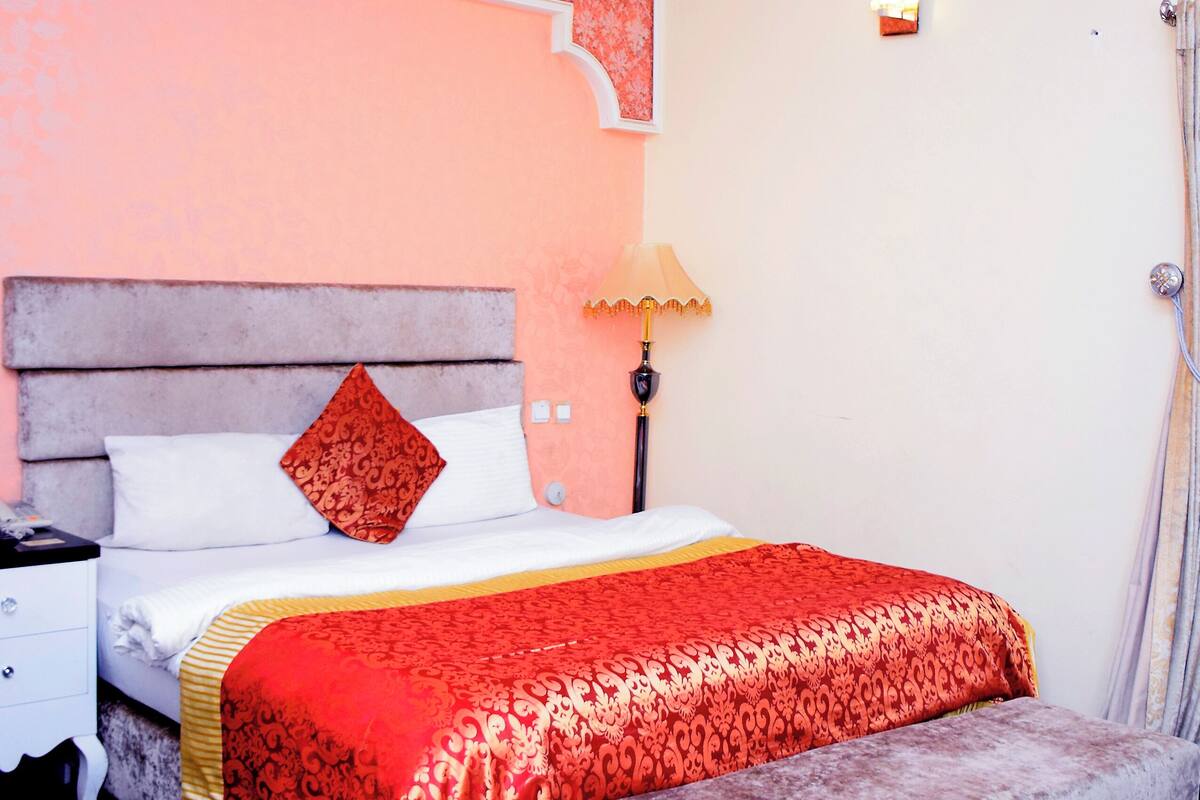 A bedroom with a bed, bedside table, lamp, and bench.