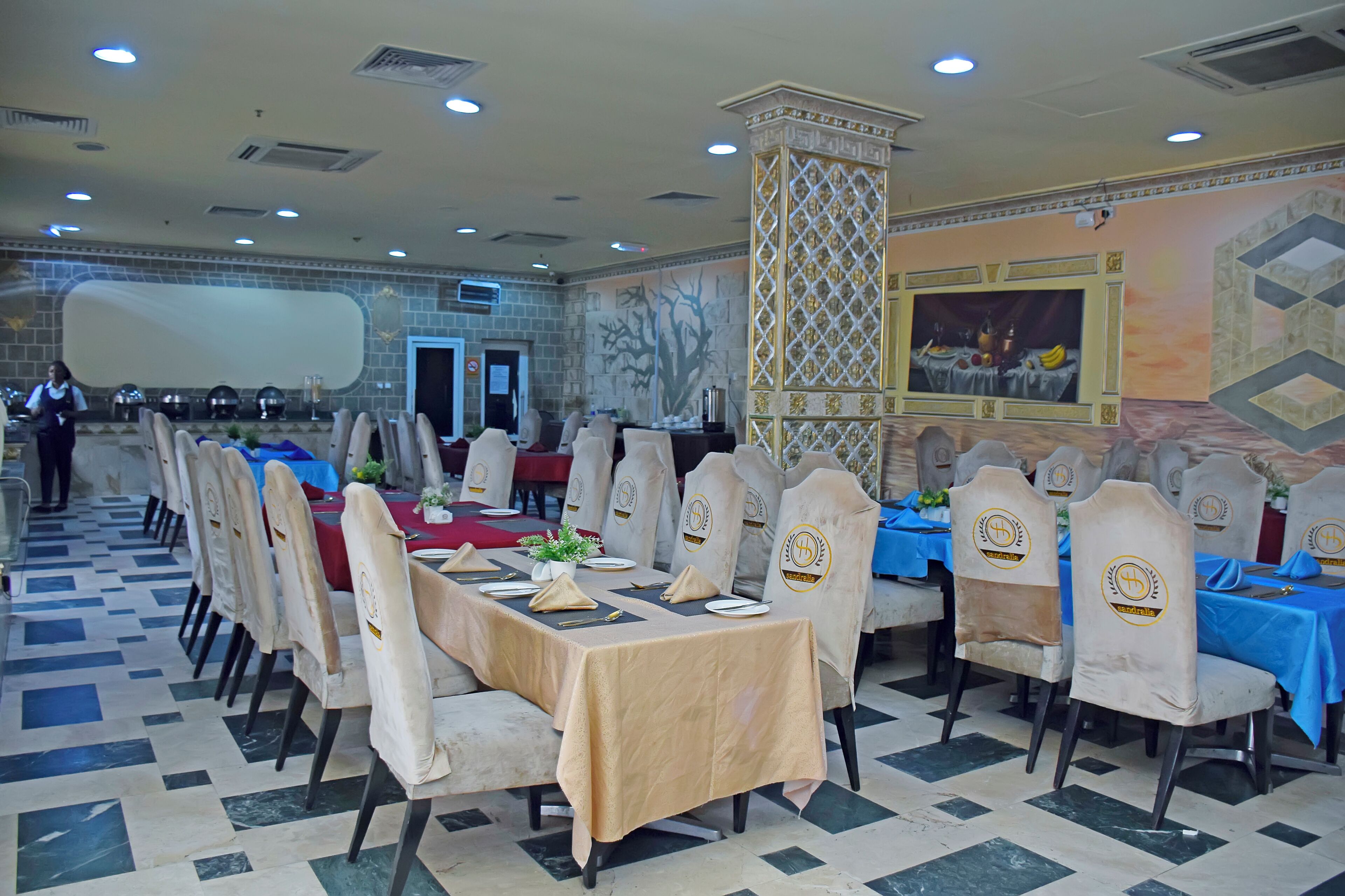 A banquet hall with tables set for dining, chairs with headrests, and a decorative wall mural.