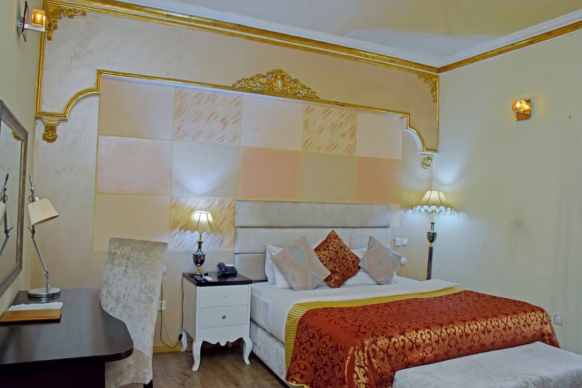 A hotel room with a large bed, two bedside lamps, a nightstand, and a desk with a lamp.