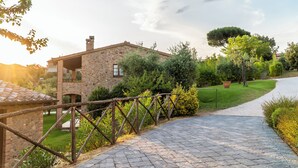 A stone house with a paved driveway, surrounded by greenery and a wooden fence. - PanElios Borgo Vacanze (Citta della Pieve)