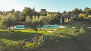 A swimming pool surrounded by grass and trees, with a fence and lounge chairs. - PanElios Borgo Vacanze (Citta della Pieve)