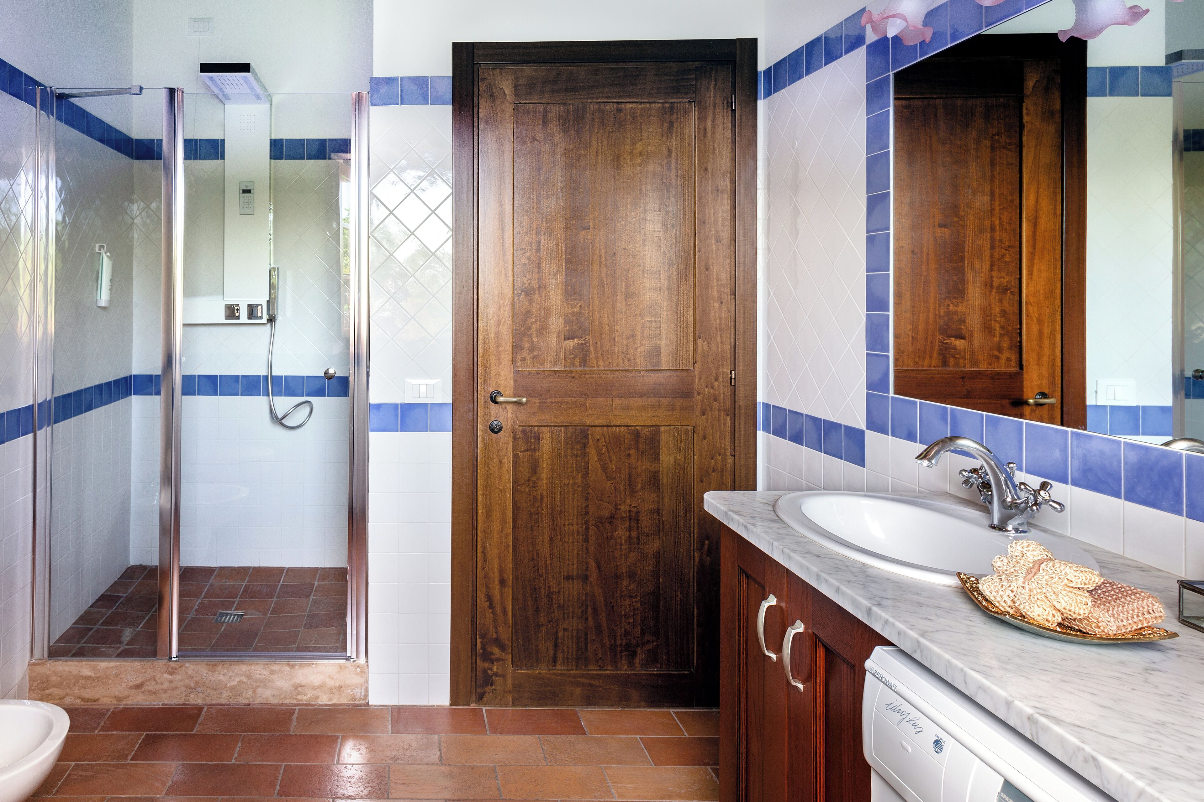A bathroom with a wooden door, a glass shower enclosure, a sink with a marble countertop, and a towel rack.