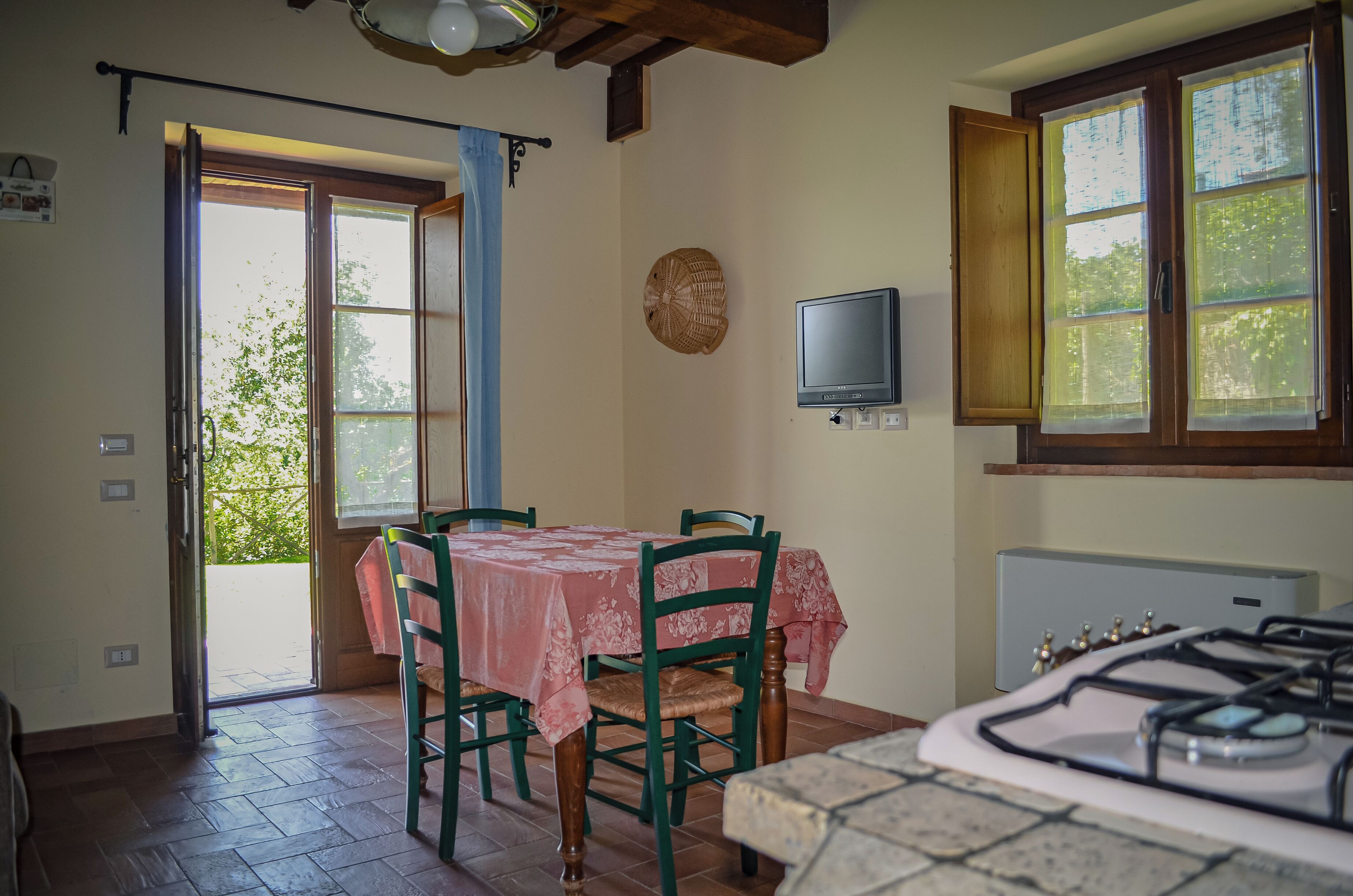 Un comedor con una mesa y sillas, un televisor montado en la pared y una ventana con cortinas.