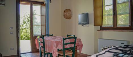 Un comedor con una mesa y sillas, un televisor montado en la pared y una ventana con cortinas.