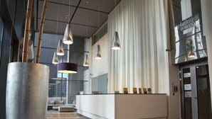 A modern reception area with a white reception desk, hanging pendant lights, and a large cylindrical planter. - Chopin Apartments Platinum Towers (Warsaw)