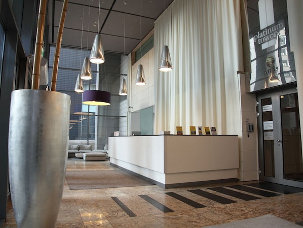 A modern reception area with a white reception desk, hanging pendant lights, and a large cylindrical planter.