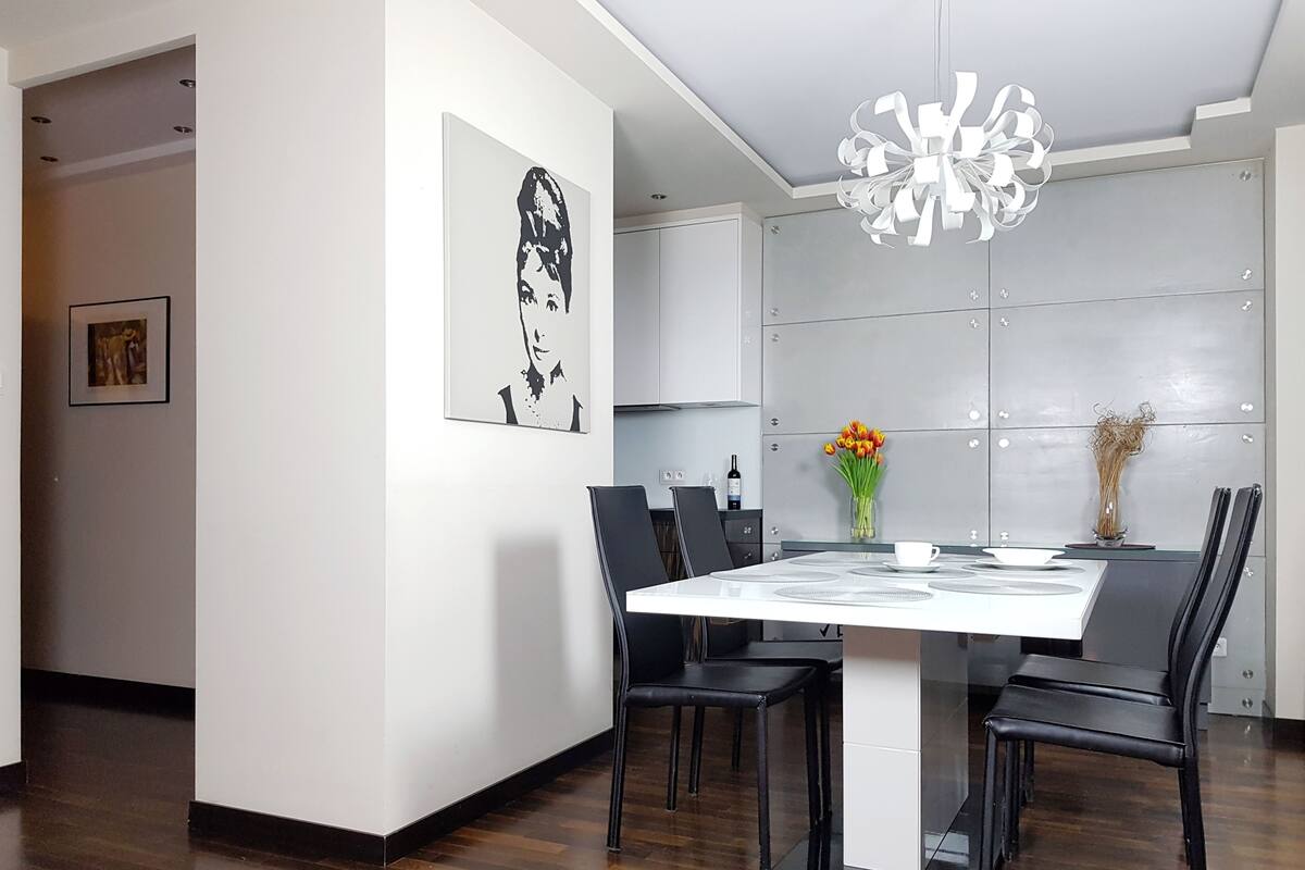 Un espace de salle à manger moderne avec une table blanche, des chaises noires, un lustre et des œuvres d’art accrochées aux murs.